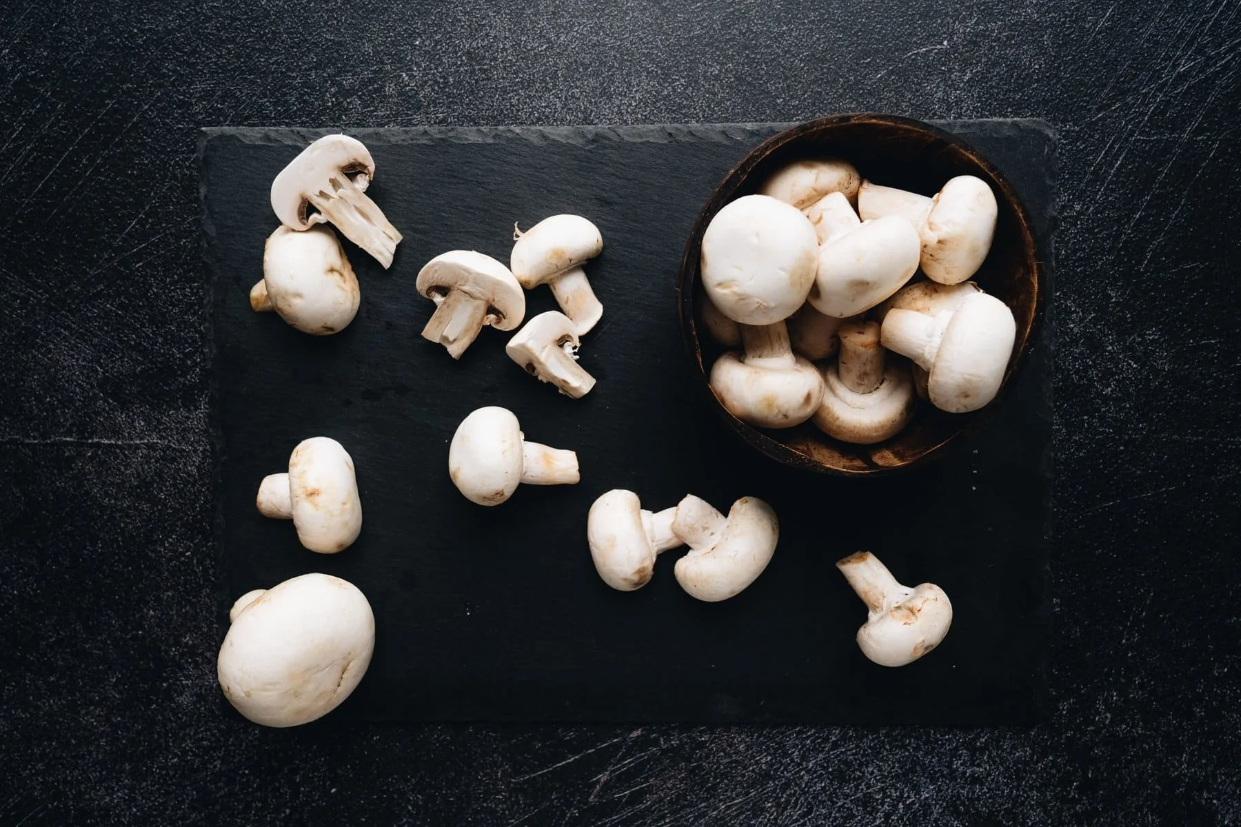 Button mushrooms arranged on a dark surface